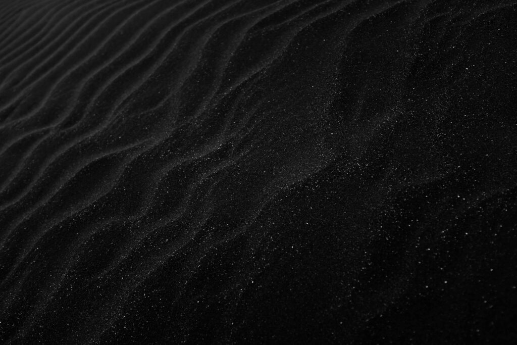 Textured black sand with ripples resembling dunes, creating a dark, abstract aesthetic.